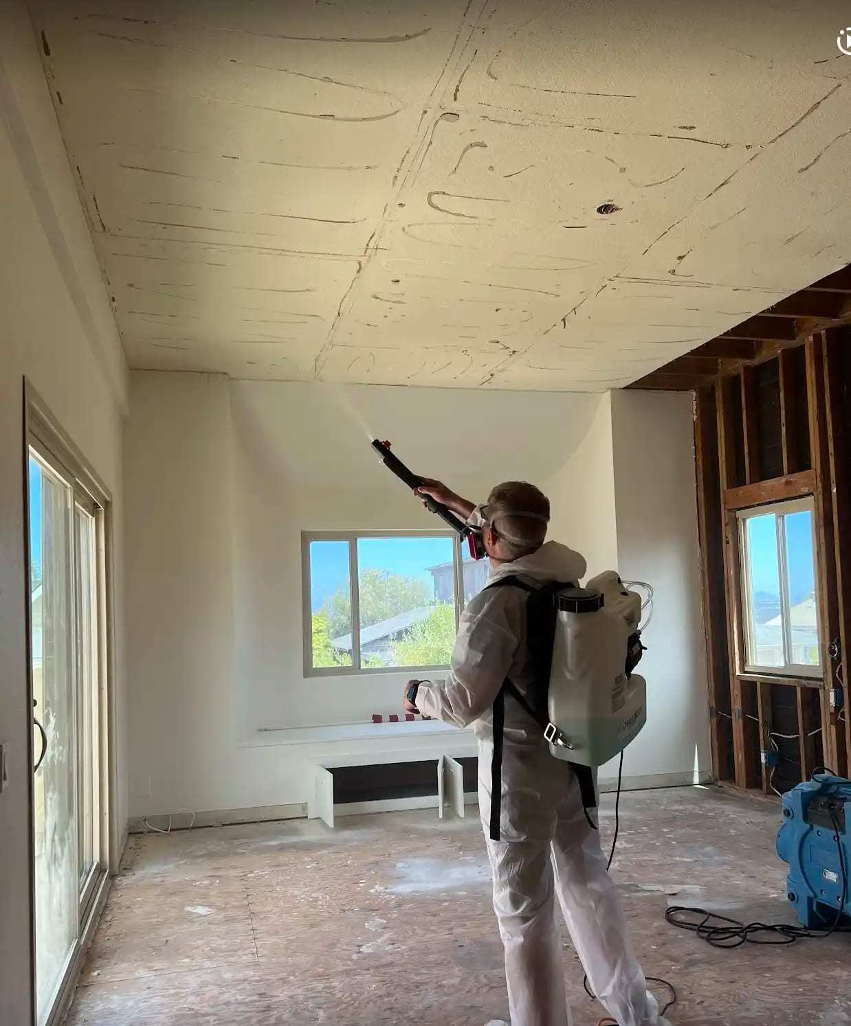 Technician with a backpack sprayer treating a room stripped to the framing