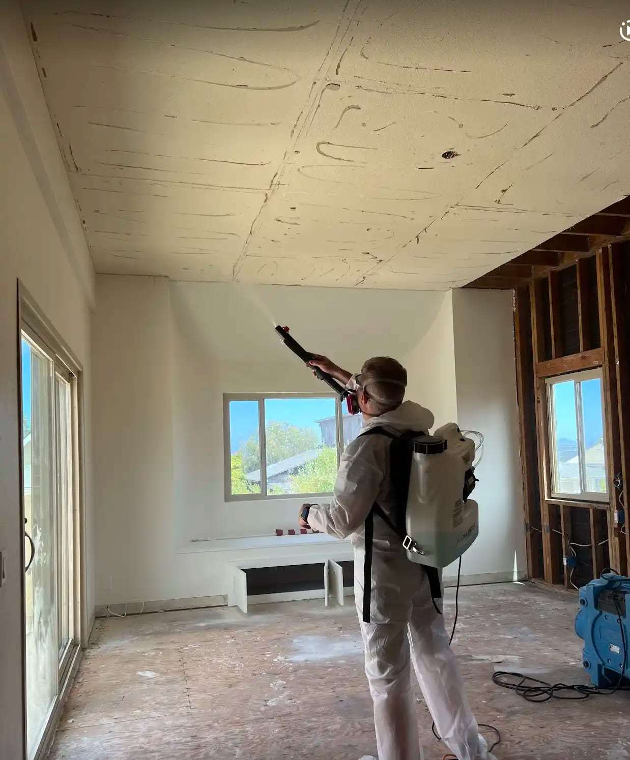 Technician with a backpack sprayer treating a room stripped to the framing