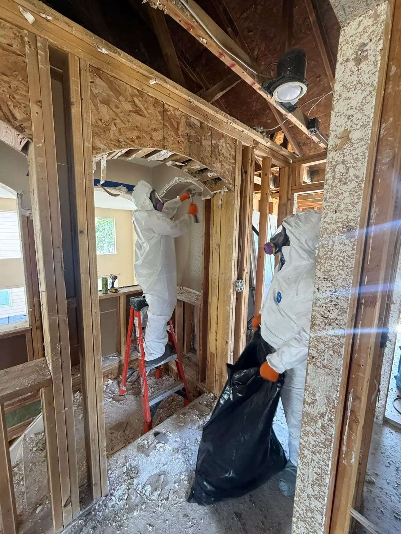 Technicians in protective suits removing debris from an attic opened to the framing