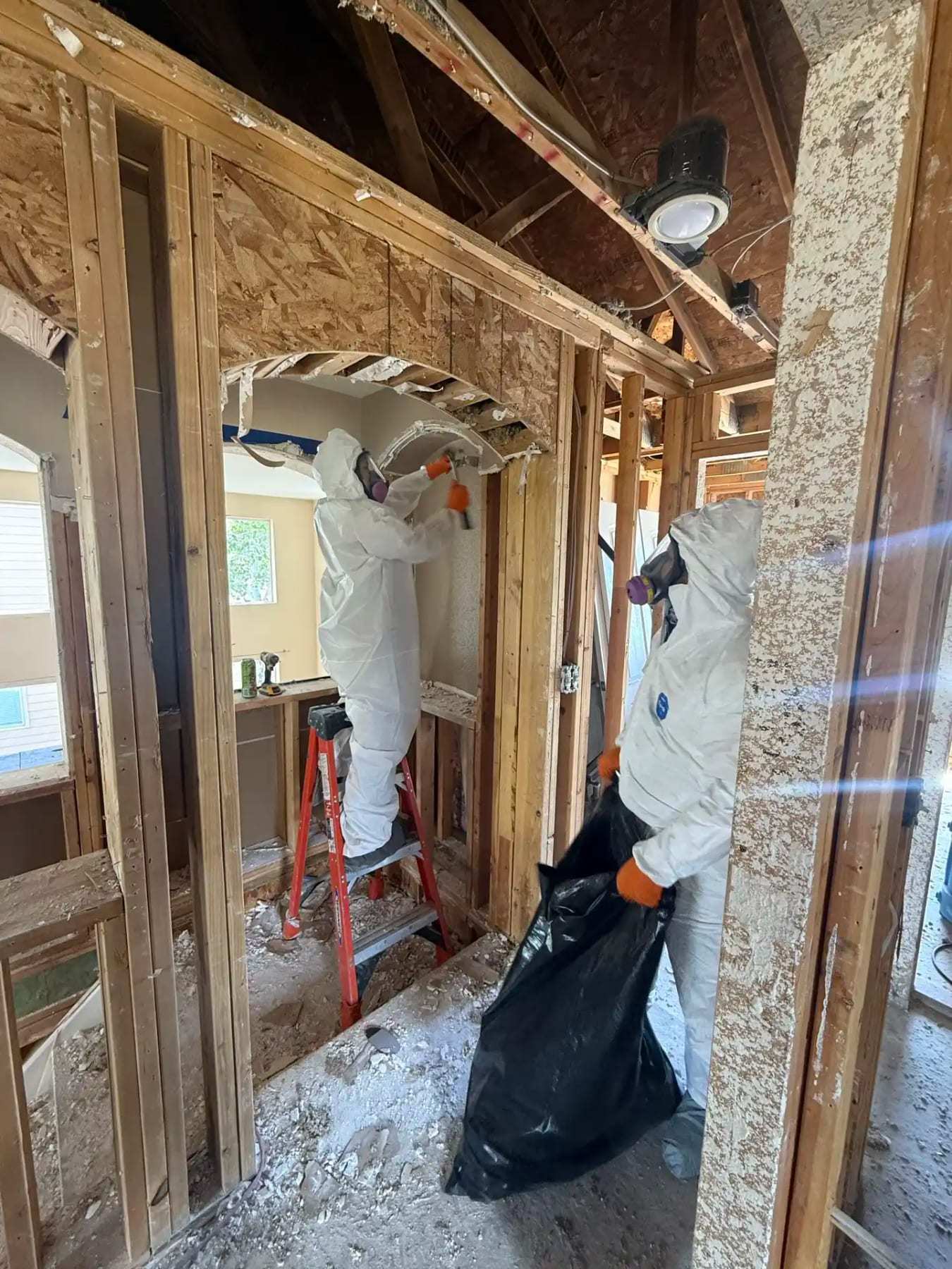 Technicians in protective suits removing debris from an attic opened to the framing
