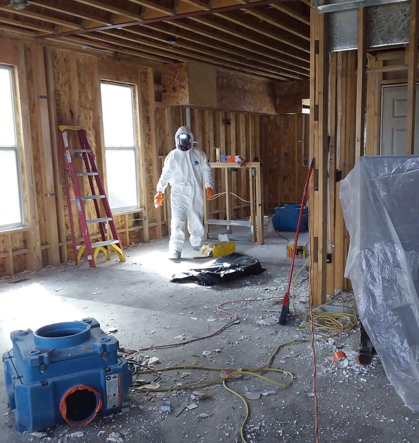 Technician in a protective suit inside a room stripped to the studs with an air mover
